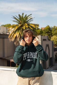 man standing on roof top wearing khaki tan pants and upper park clothing's pine green college town 3.0 hoodie whileholding both sides of the hood standing in front of palm trees and fluffy clouds photograph taken in chico california chico state norcal butte county Screen Printing Shops, Street Fits, University Style, College Town, Shirt Print Design, Fast Forward, Pine Green, Hooded Pullover, Heavy Weight