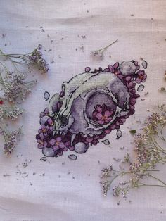 some flowers and plants on a white cloth with purple thread work in the middle,