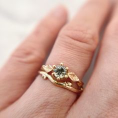 "Handcrafted from a delicate budded twig, the Flora Solitaire Band is adorned with thyme leaves and features a mint green Montana Sapphire in a 6-prong setting.  100% recycled gold  100% ethically-sourced Montana Sapphire Every single ring in my collection is designed, sculpted and produced entirely by hand. I never use computers and I never use \"off-the-shelf\" designs that you see in so many jewelry stores. Each ring begins by casting an actual twig or piece of bark; its natural, imperfectly Leaf Engagement Ring Nature, Engagement Rings Organic, Green Engagement Rings, Contour Ring, Green Montana, Solitaire Bands, Nature Engagement Ring, Montana Sapphire Ring, Sapphire Solitaire Ring