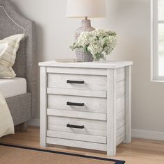 a white nightstand with flowers on it next to a night stand and a bed in the background