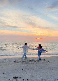 two people on the beach holding hands and dancing in front of the ocean at sunset