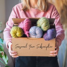 a woman holding a box filled with balls of yarn and the words seasonal yarn sale written on it