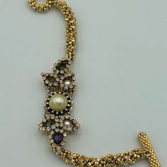 a gold necklace with pearls and other jewels on it's side, in the shape of a cross