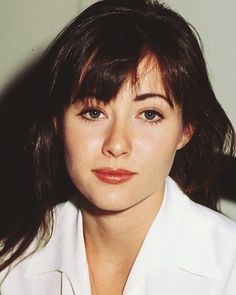 a close up of a person wearing a white shirt and looking at the camera with a serious look on her face