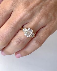 a woman's hand holding an engagement ring with two baguettes on it