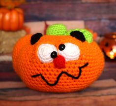 a crocheted orange with a face on it sitting on a table next to pumpkins