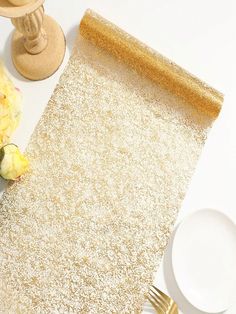 a white table topped with gold glitter paper next to a plate and cup filled with flowers