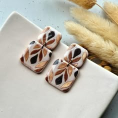 two square shaped ceramic pieces sitting on top of a white plate next to dried grass