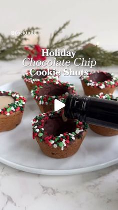 chocolate cupcakes with sprinkles are on a white plate next to a bottle of wine