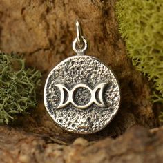 two fish are sitting in the middle of a circle pendant on a tree branch with moss growing around it