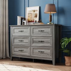 a gray dresser in a blue room next to a lamp