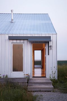 a small white house sitting on top of a grass covered field next to a wooden walkway