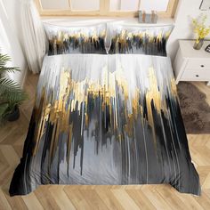 a bed with black and gold comforter covers on top of wooden flooring next to a window