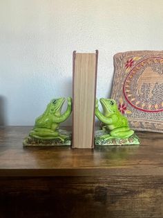 two green frog bookends sitting on top of a wooden table