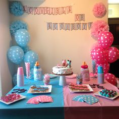 a table topped with cake and balloons next to a wall filled with blue and pink decorations