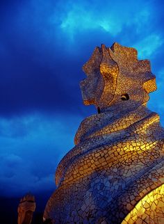 the top of a building that is lit up at night with blue sky and clouds in the background