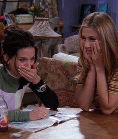 two young women sitting at a table with papers on it and one woman covering her mouth