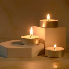 three lit candles sitting on top of a white block in front of a beige wall