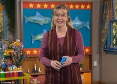 a woman standing in front of a tv screen holding a blue object and smiling at the camera