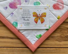 a pink and white bib with a butterfly design on it, sitting on top of a wooden surface