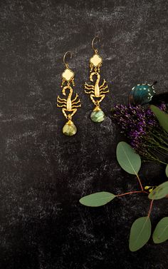 two pairs of earrings sitting on top of a black surface next to flowers and leaves