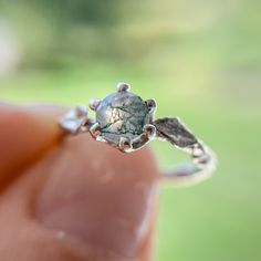 a close up of a person's hand holding a ring with a stone in it