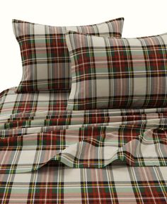 a bed with plaid sheets and pillows on top of it, in front of a white background