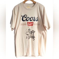 Coors Banquet Beer T-Shirt Featuring A Cowboy With Lasso & Horse Pencil Drawing. Intentionally Distressed For A Vintage Vibe. Text Reads "Coors Banquet" "Golden Colorodo" "Est 1873". A Simple, Pleasant Design On A Delightfully Oatmeal-Colored Shirt. Official Coors Licensed Product Printed On A Quality Teeluv Shirt. 100% Cotton. New With Tag. American Golden Mountains Lager Alcohol Usa Co U.S.A. U.S. United States Of America Alcoholic Bar Beverage Golden Colorado Bar Drinking Games Pbr College Pong Dad Humor Party Fun Pub Garden Oktoberfest Brewery Microbrewery America Alcohol Budweiser Bud Moon Natural Light Michelob Ultra Anheuser-Busch Miller High Life Yuengling Pabst Blue Ipa Bier Ri Retro Cream Short Sleeve T-shirt, Vintage Cream Tops With Letter Print, Vintage Cream Short Sleeve T-shirt, Retro Beige Crew Neck T-shirt, Beige Retro Crew Neck T-shirt, Cream Vintage T-shirt With Relaxed Fit, Vintage Cream Crew Neck T-shirt, Vintage Cream T-shirt For Summer, Vintage Short Sleeve Cream T-shirt