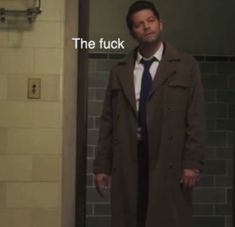 a man in a coat and tie standing in front of a bathroom door with the caption, the fock