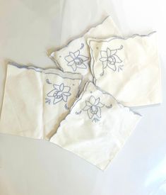 three napkins with embroidered flowers on them sitting on a white tablecloth covered surface