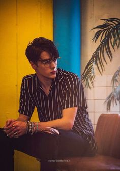 a young man sitting on top of a brown chair next to a potted plant