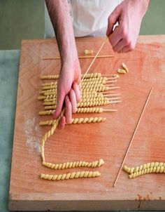 a man is making pasta on a wooden cutting board with toothpicks in it