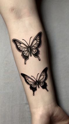 two butterfly tattoos on the wrist and arm, one is black with white butterflies in it