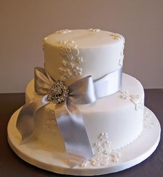 a three tiered wedding cake with silver ribbon and flowers on top, sitting on a table