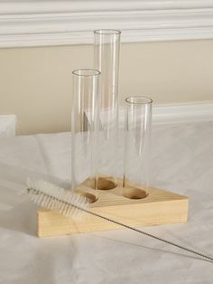 three tall clear vases sitting on top of a wooden tray next to a feather