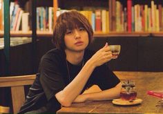 a person sitting at a table with a cup in front of him and bookshelves behind them