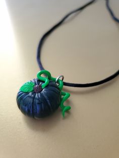 a necklace with a blue shell and green leaves on it sitting on a white surface