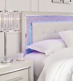 a white bed topped with pillows next to a night stand filled with crystal candles and lights