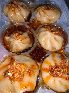 there are many dumplings in the plastic container with sauce on them and toppings