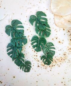 two green leafy earrings sitting on top of a table