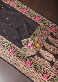 an embroidered black cloth with pink and green flowers on the border is laying on a wooden floor