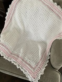 a white crocheted blanket sitting on top of a chair next to a pillow