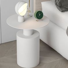 a white table sitting on top of a bed next to a night stand with a clock