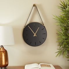 a clock hanging on the wall next to an open book and potted plant with a lamp