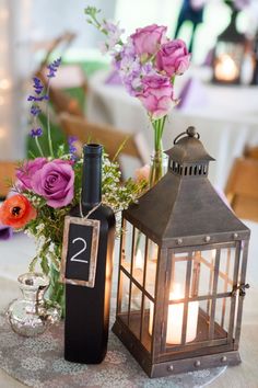 a table topped with a lantern and flowers next to a vase filled with purple flowers