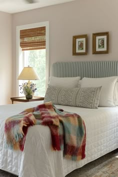 a bed in a bedroom with two framed pictures on the wall and a blanket draped over it