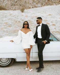 a man and woman standing next to a white car