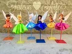 four tinkerbell fairy figurines sitting on top of each other in front of a brick wall