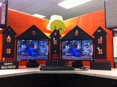 two computer monitors sitting on top of a desk in front of an orange wall with halloween decorations