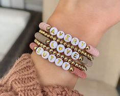 Find the gold spacer bracelets here: https://www.etsy.com/listing/1217760416/gold-bead-personalized-name-bracelet Choose your colors, your sizes, and any words/letters/names/initials/phrases! The perfect gift for yourself or someone else!  Mama-to-be / baby shower / kids names / initials Bride-to-be / new initials / bachelorette or wedding party gifts Teacher gifts / school colors / school names, teams BFF bracelets / party favors / gifts for squads, teams, clubs, sororities Motivational words, Name Clay Bead Bracelet, Custom Bracelet Ideas, Mama Bracelet Stack, Personalized Beaded Bracelets, Bead Name Bracelets, Alphabet Bracelets, Kids Name Bracelet, School Names, Bead Bracelet Stack